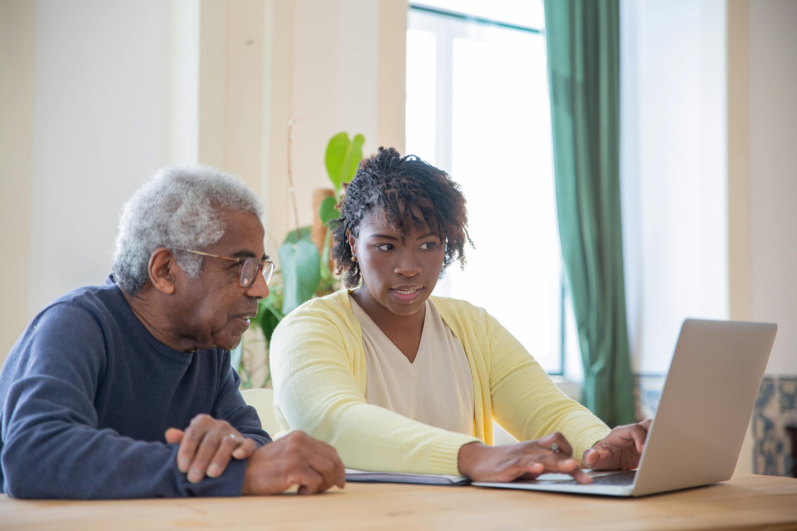 A young woman helps an older man review something on a laptop at home