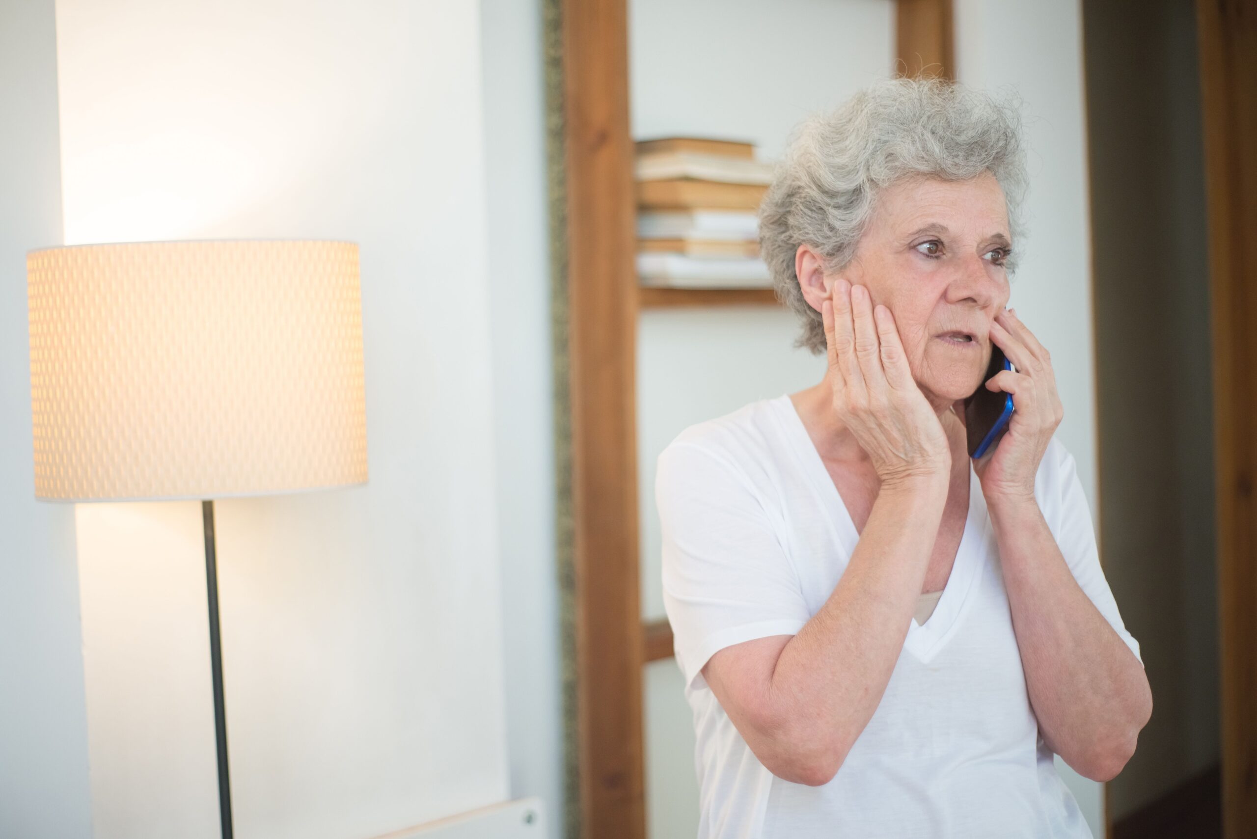 An older woman with a worried expression talks on the phone at home